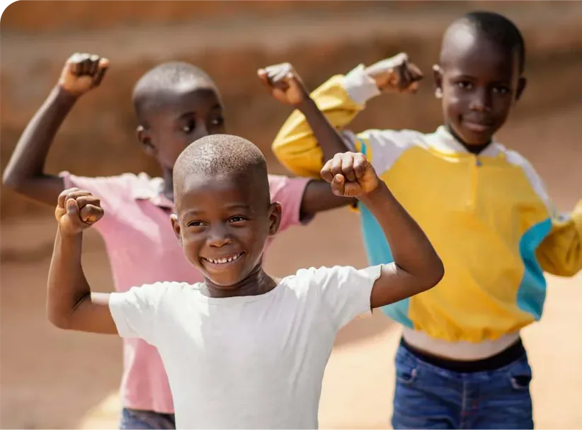 Three young boys flex their arms and smile outdoors.