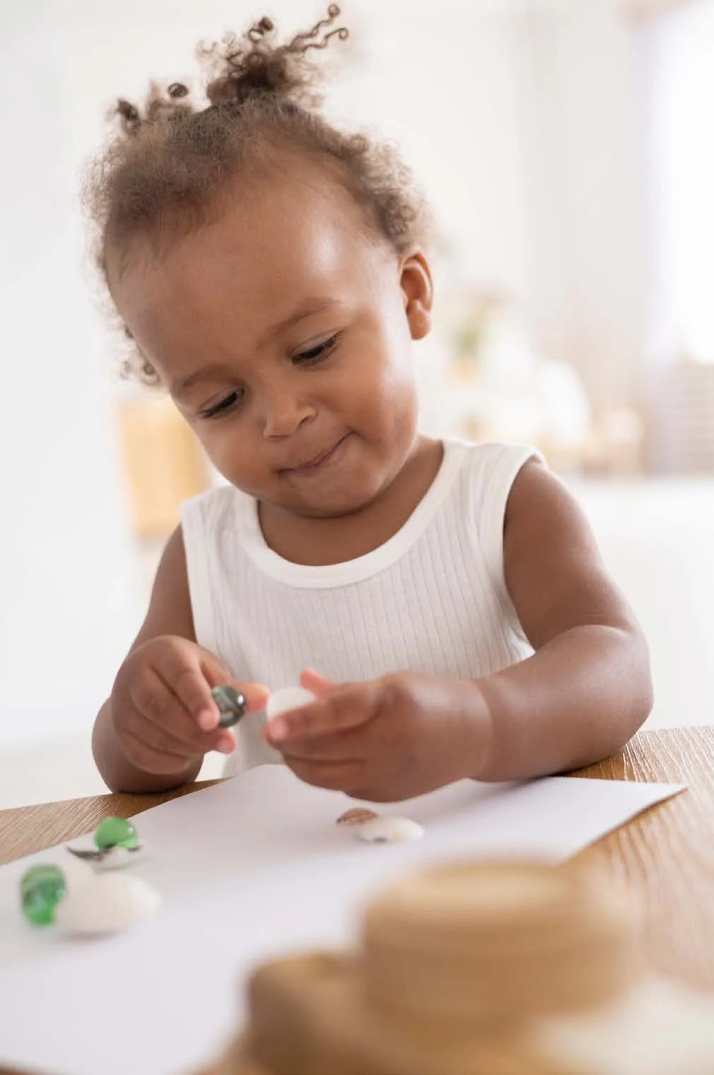 A toddler sits at a table playing with small modelling-clay shapes.