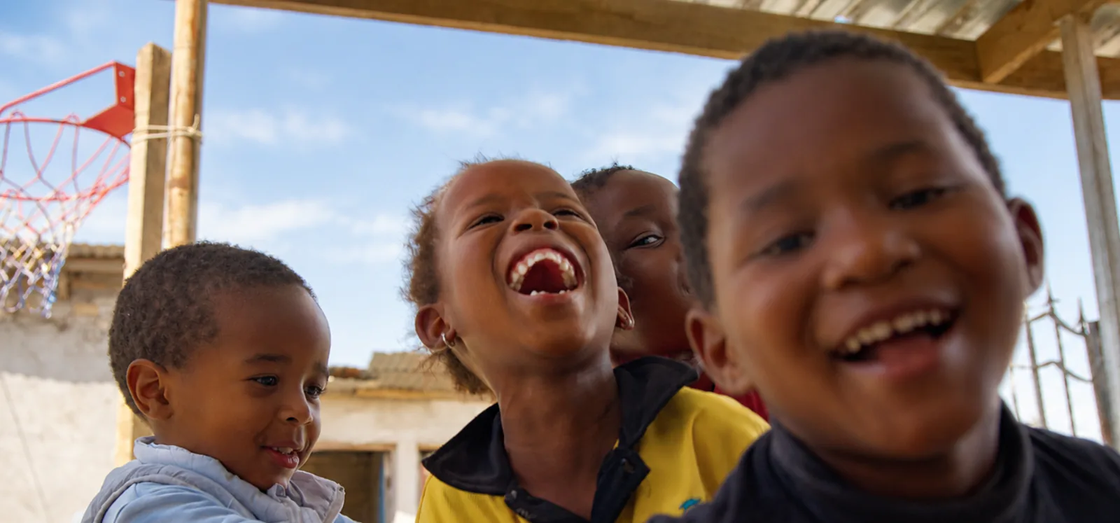 Four young children laughing together outside, with a girl in the middle.