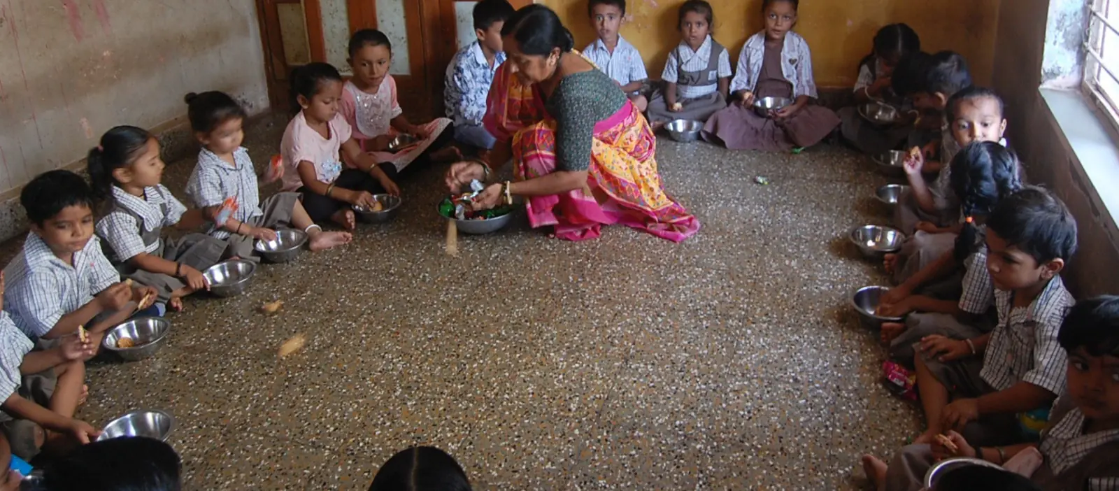 Young children sitting on the floor sharing a meal at an early learning centre in India.