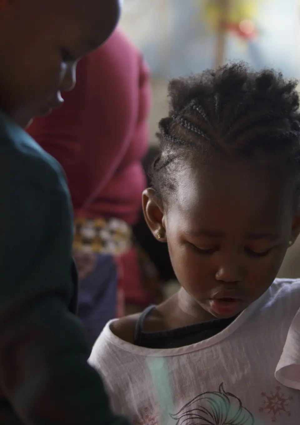 A young girl with braided hair looks down at an activity in a classroom.