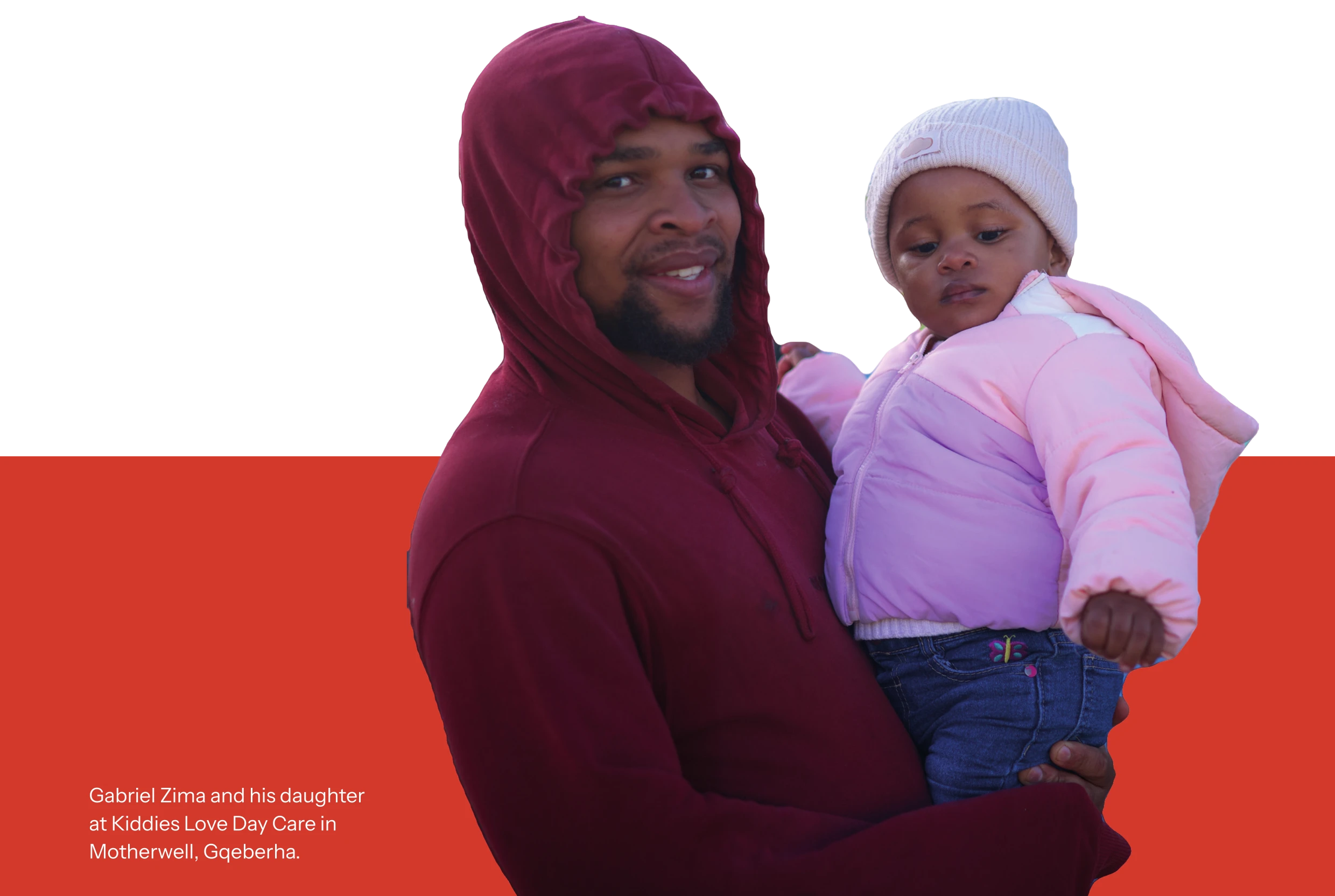 Gabriel Zima, in a red hoodie, smiling and holding his young daughter in a pink jacket and white beanie.
