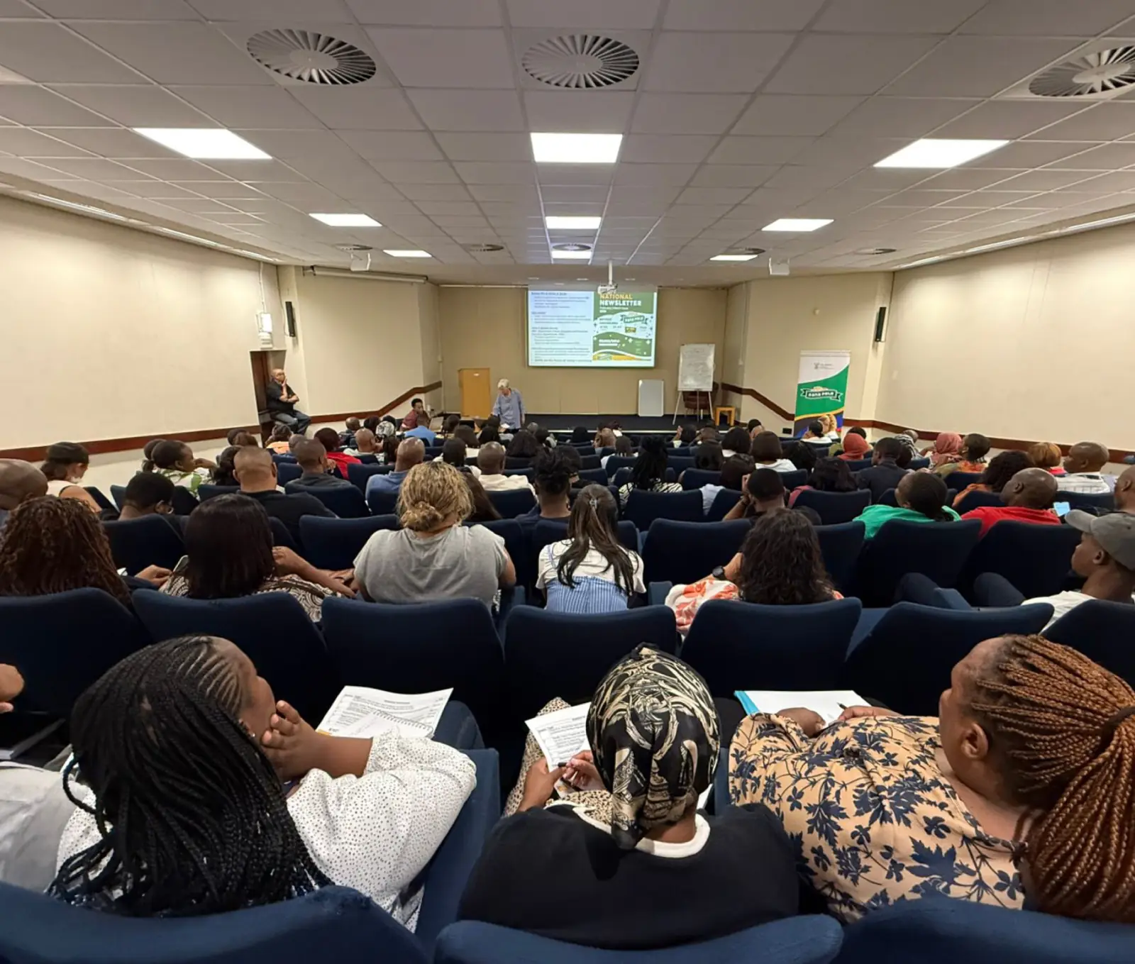A lecture hall full of workshop participants facing a presenter and a projected slide.